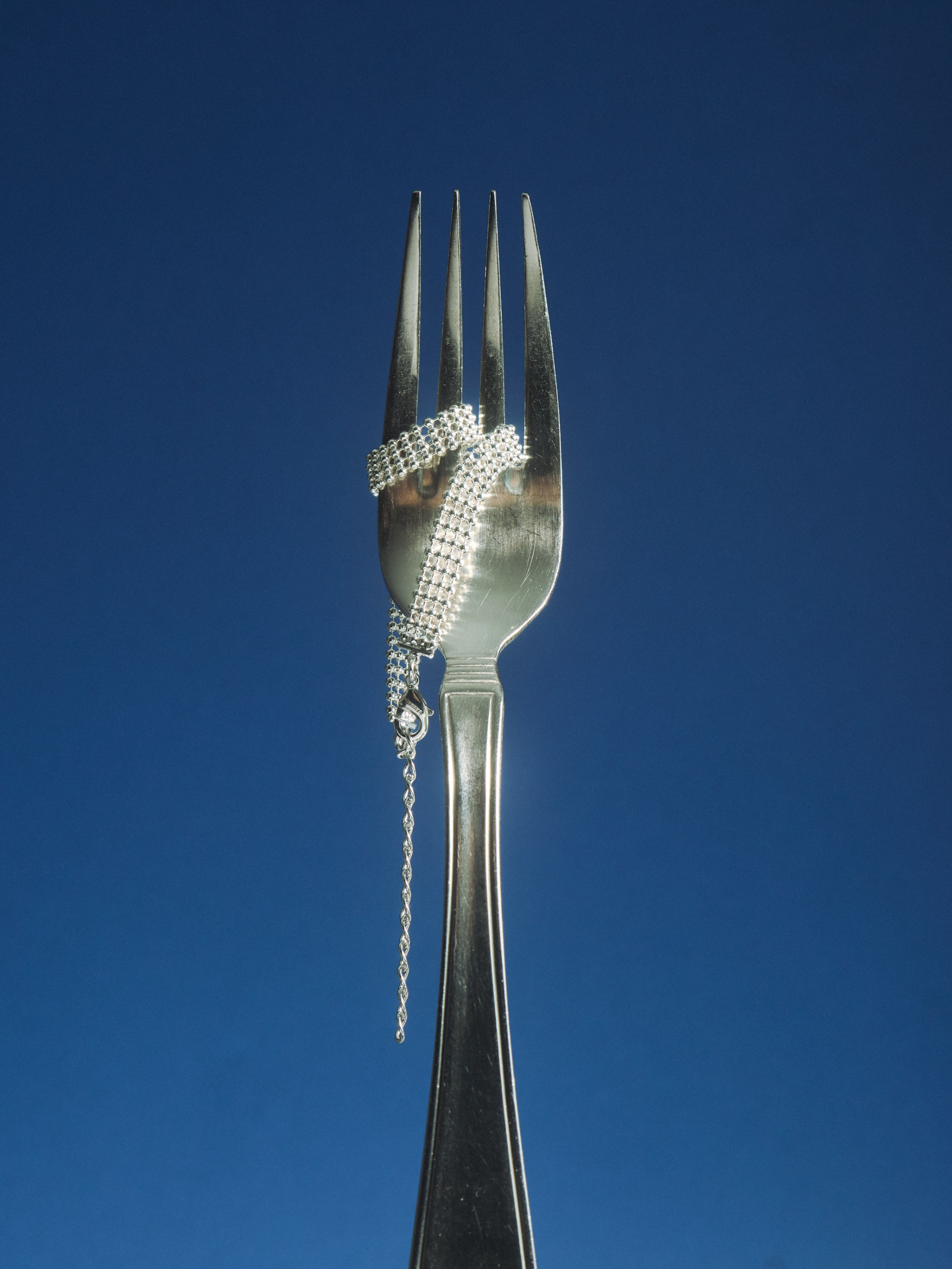 Elegant silver fork with a sparkling beaded chain wrapped against a deep blue backdrop.