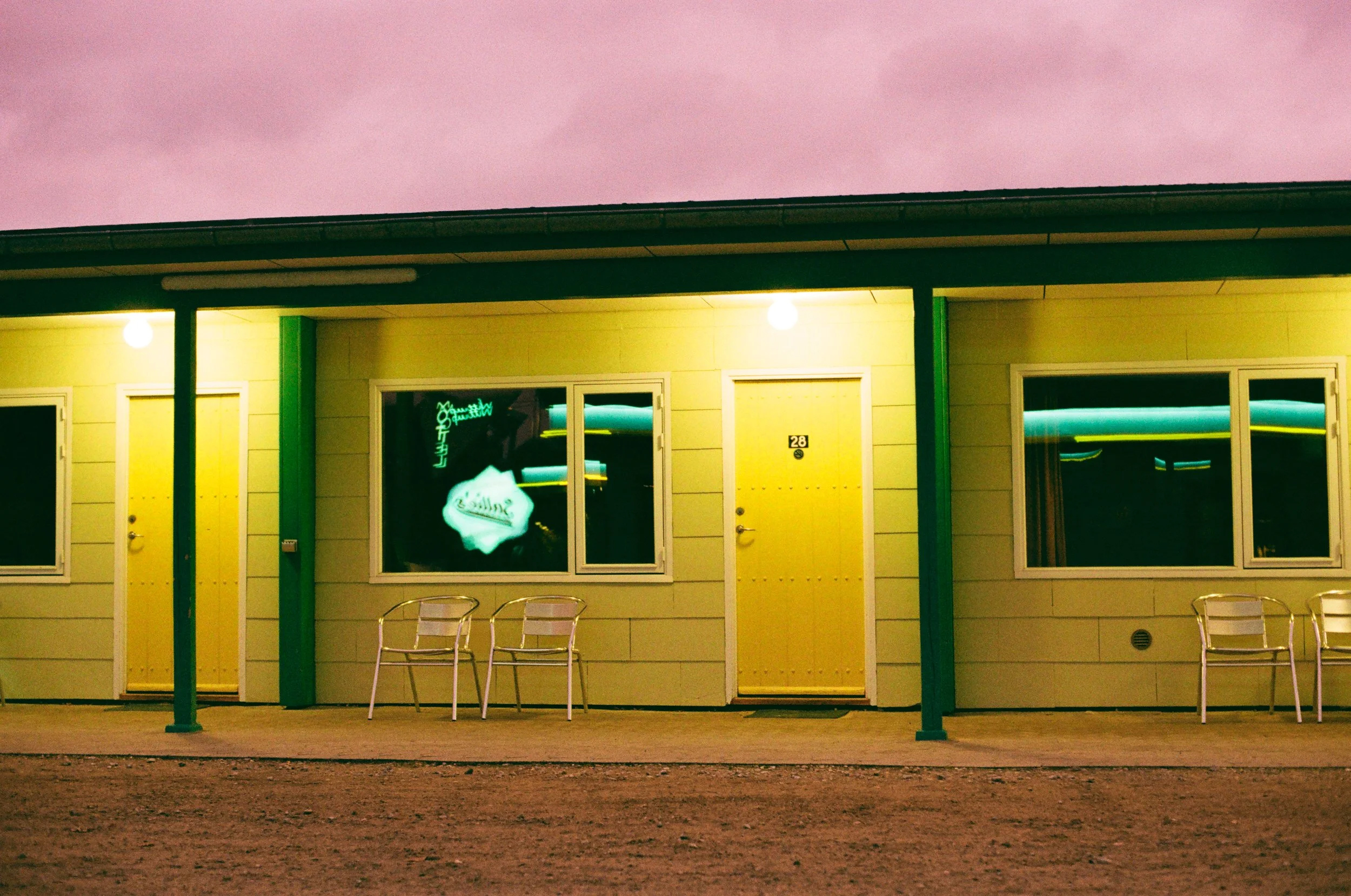 Colorful motel exterior with yellow doors, green columns, and a bright pink sky.