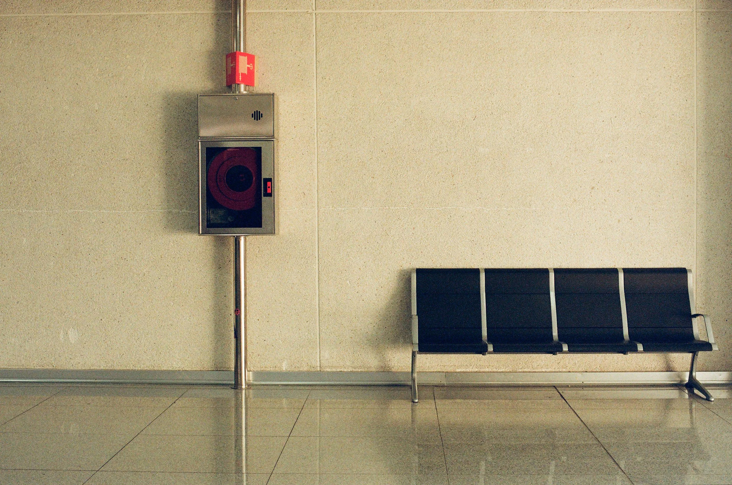 Stainless steel fire hose cabinet and black waiting chairs in a modern, empty waiting area.