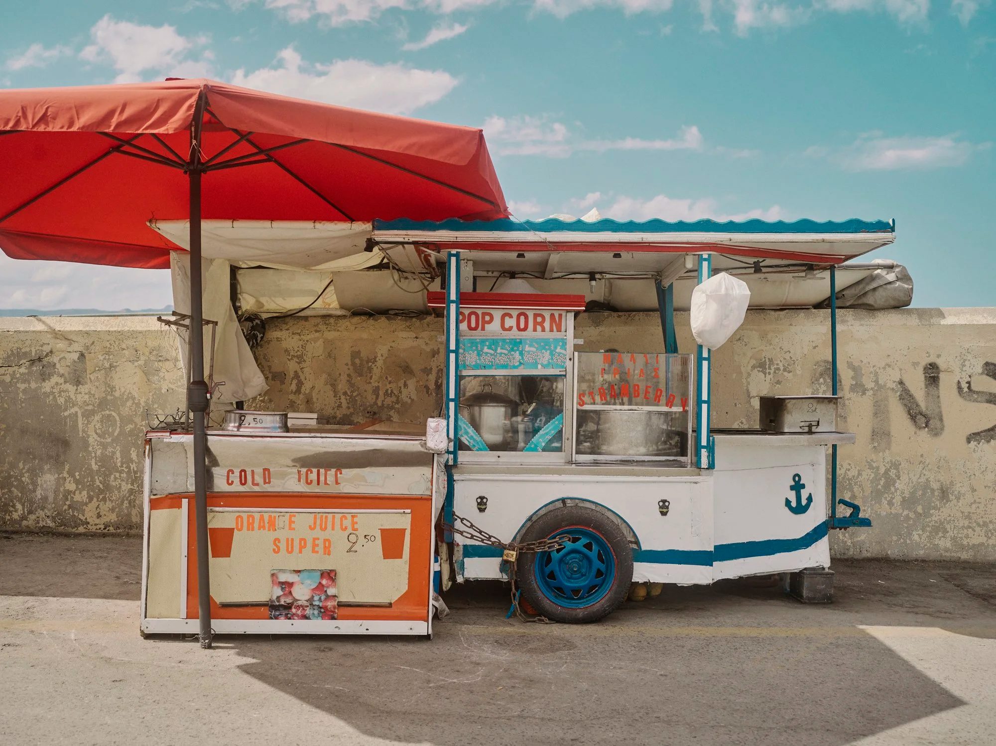 A red umbrella shades a retro-style food truck with 'POP CORN' and 'ORANGE JUICE' signs.