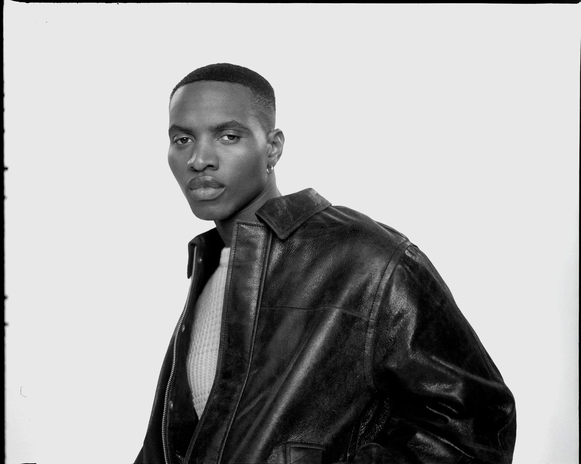 Black and white portrait of a man in a black leather jacket and sweater, looking at camera.