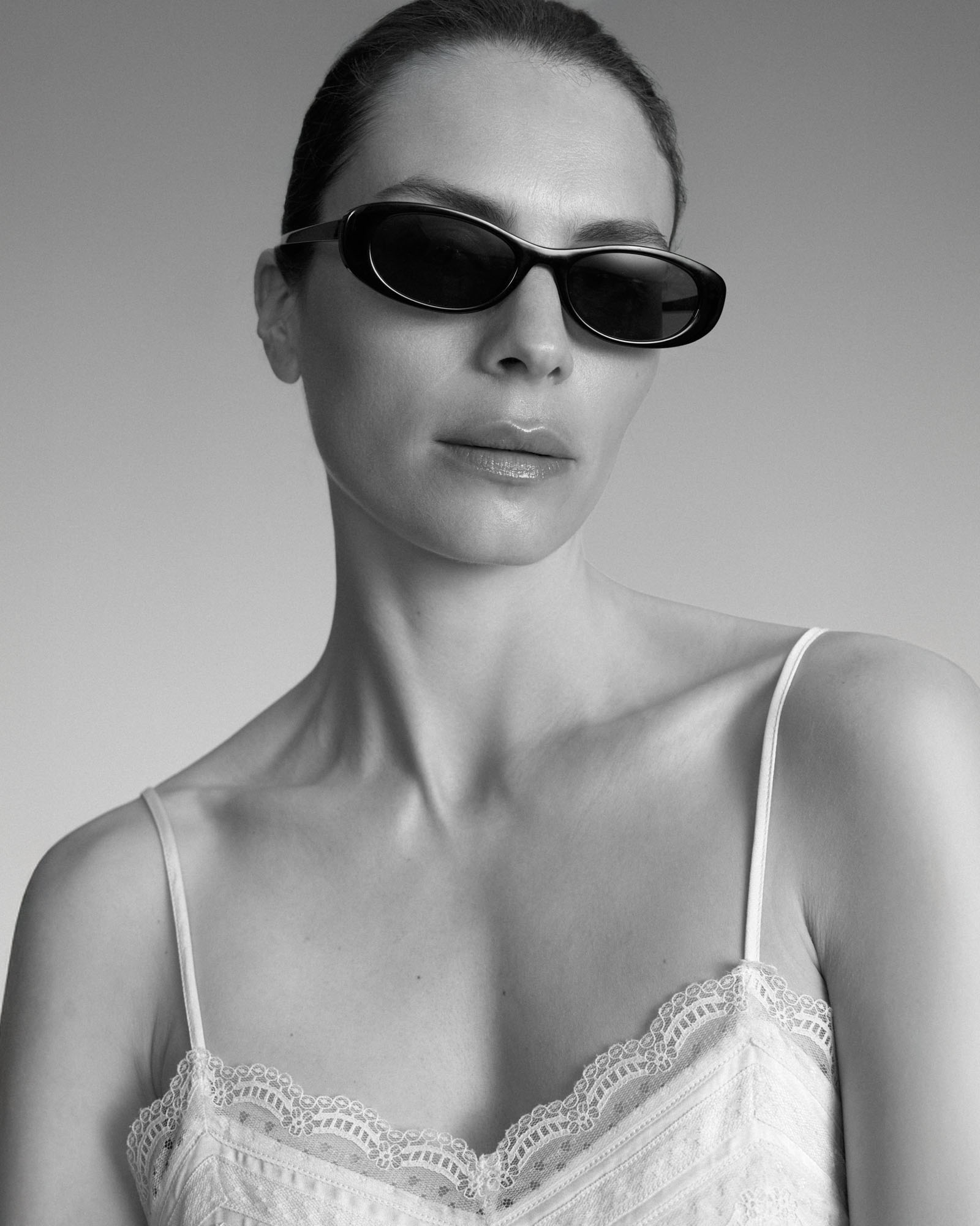 Black and white portrait of a woman wearing black sunglasses and a white lace camisole.