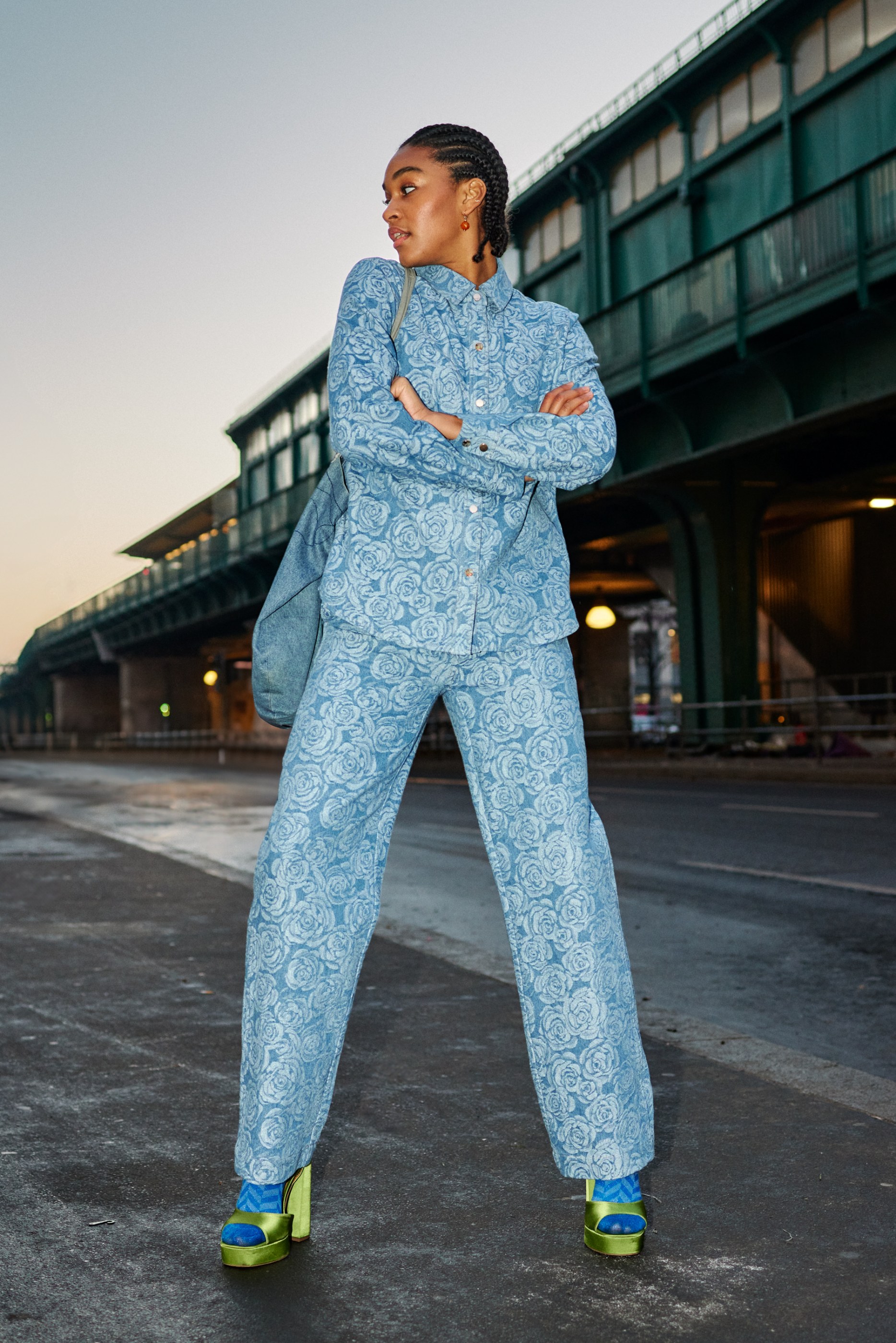Woman in rose-patterned blue denim outfit and green platform sandals on an urban street.