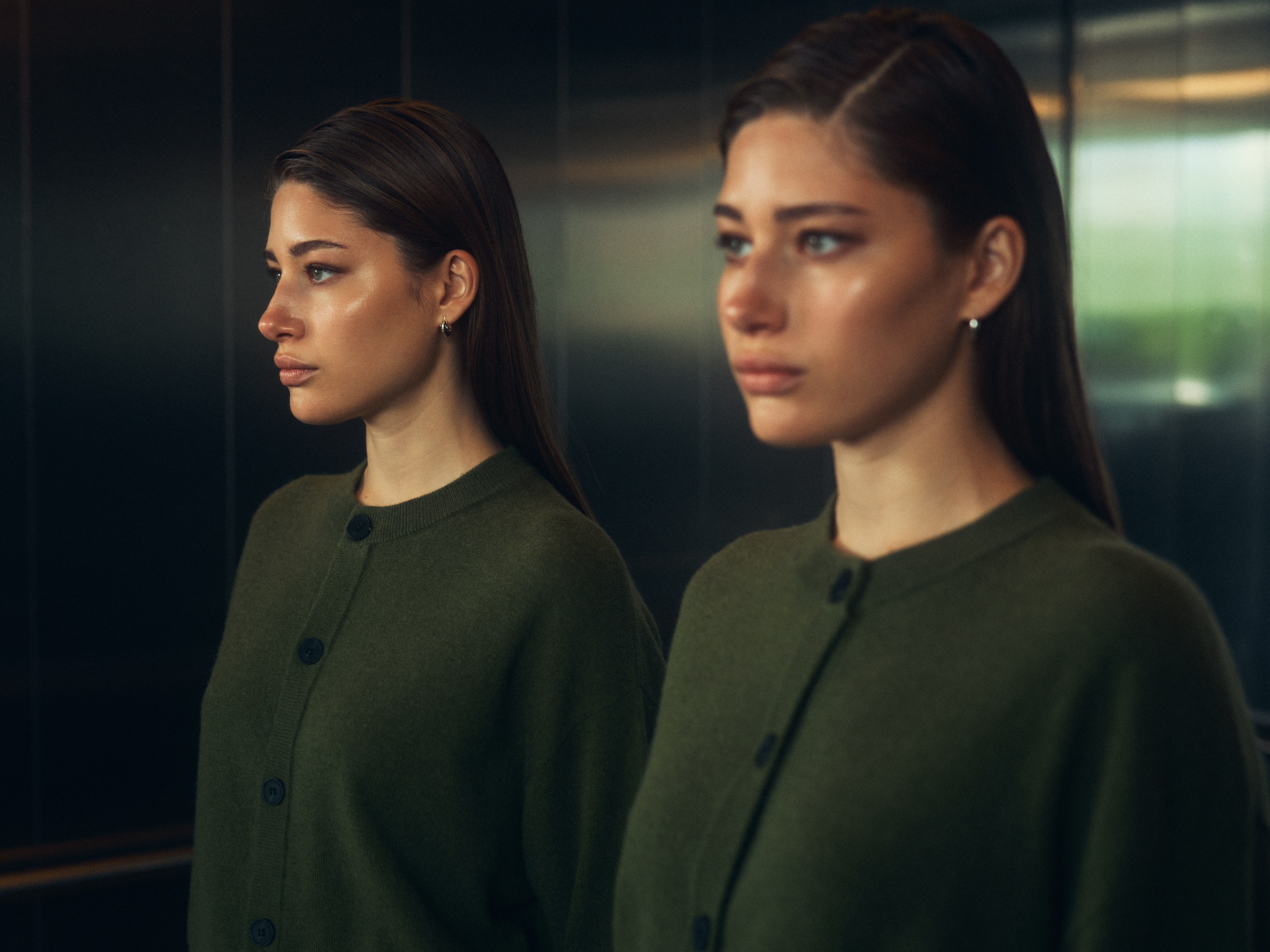 Two similar women in green cardigans, looking left, in a dark, softly lit interior.