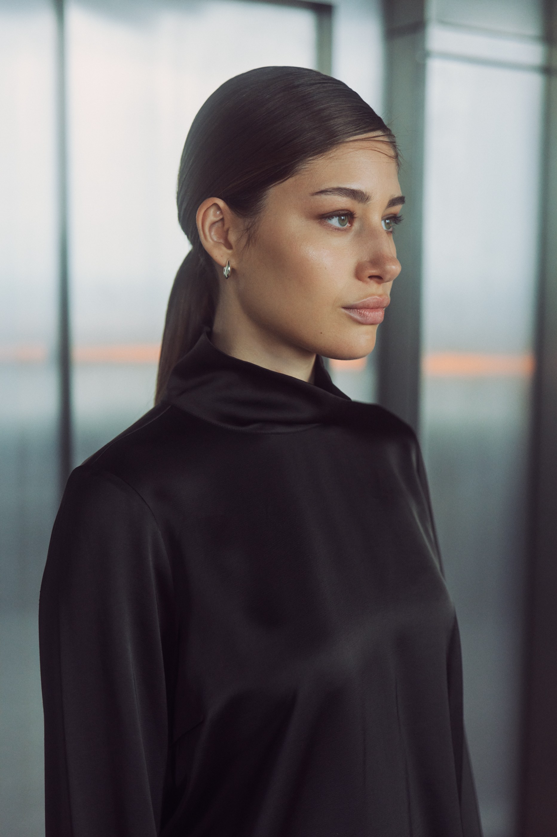 Woman with sleek hair in black high-neck top, side profile, soft light.