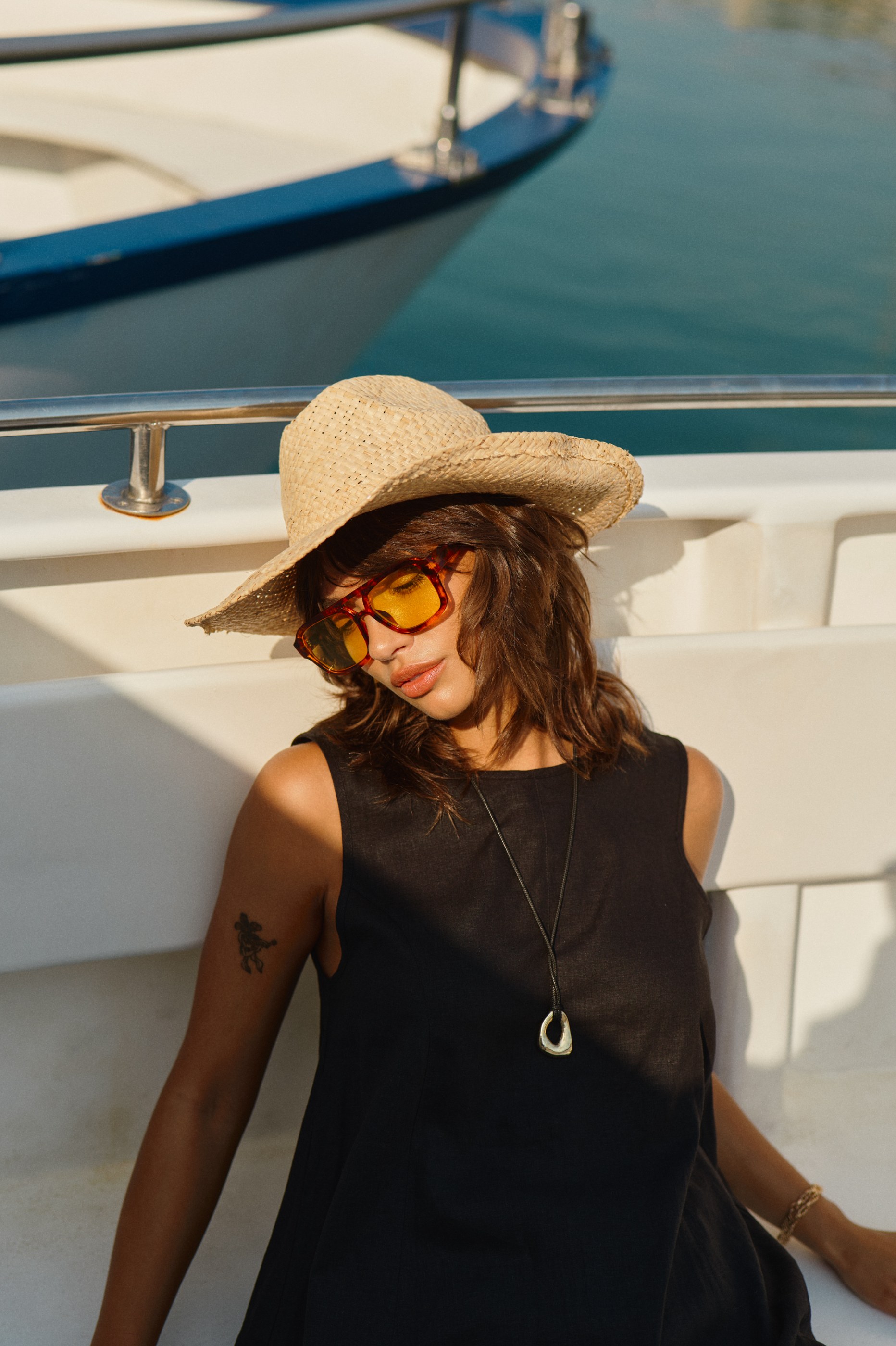 Relaxed woman in straw hat, yellow sunglasses, and black top on a boat