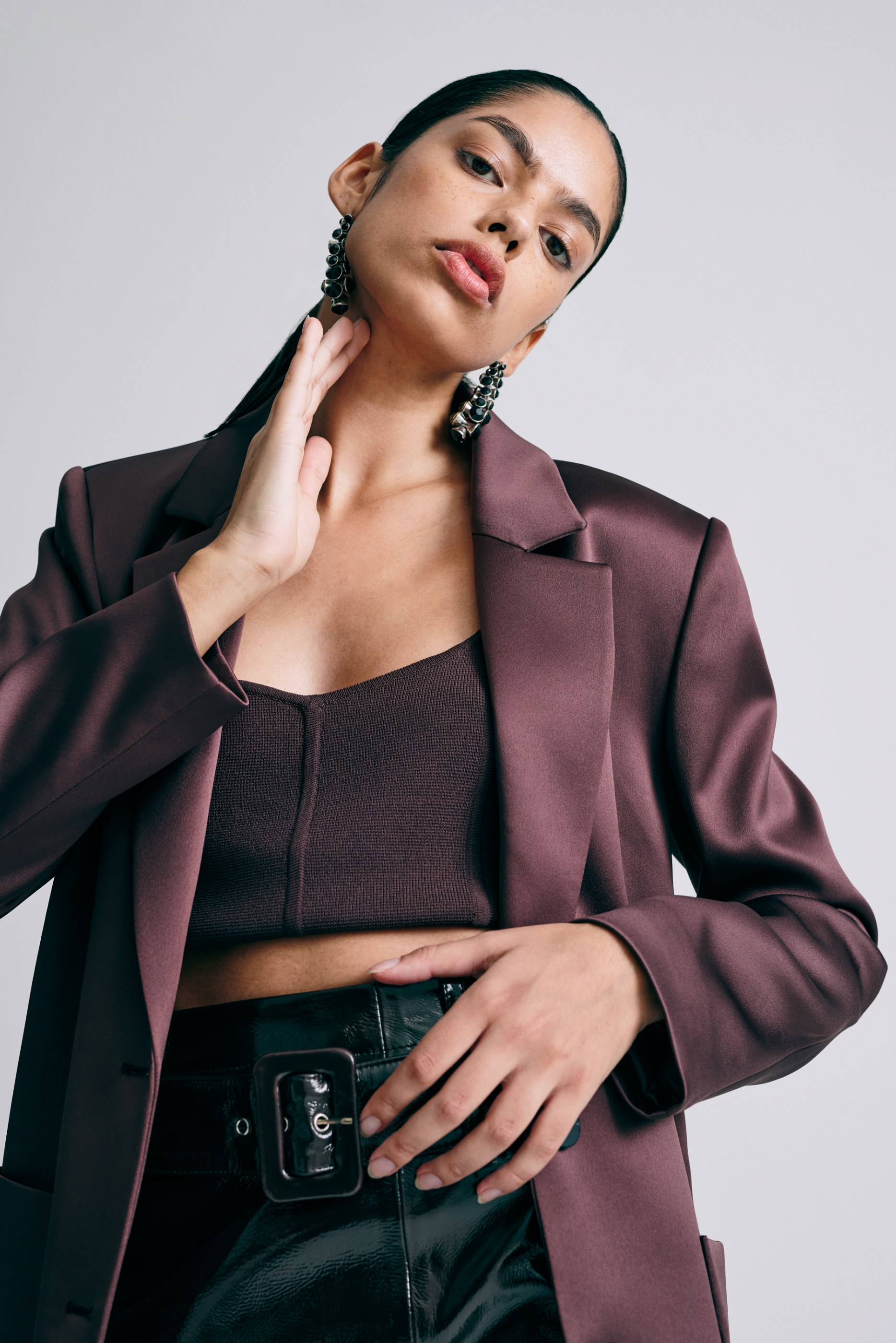 Fashionable woman wears a plum satin blazer, dark crop top, and black patent skirt.