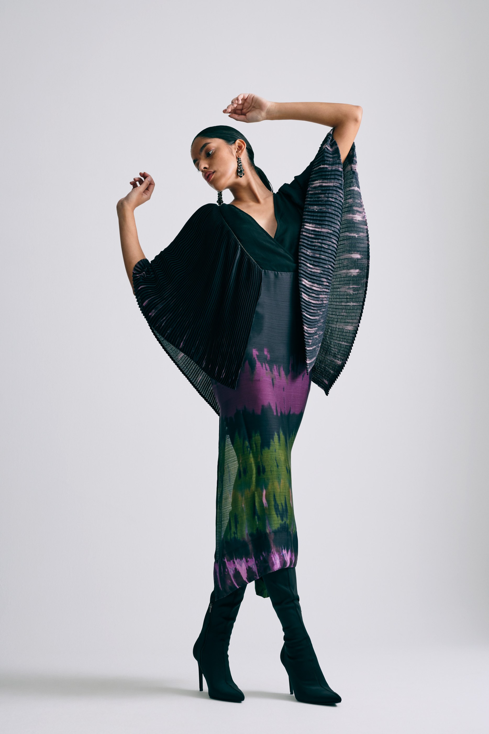 Fashion model poses in a pleated and tie-dye dress with black high-heeled boots.