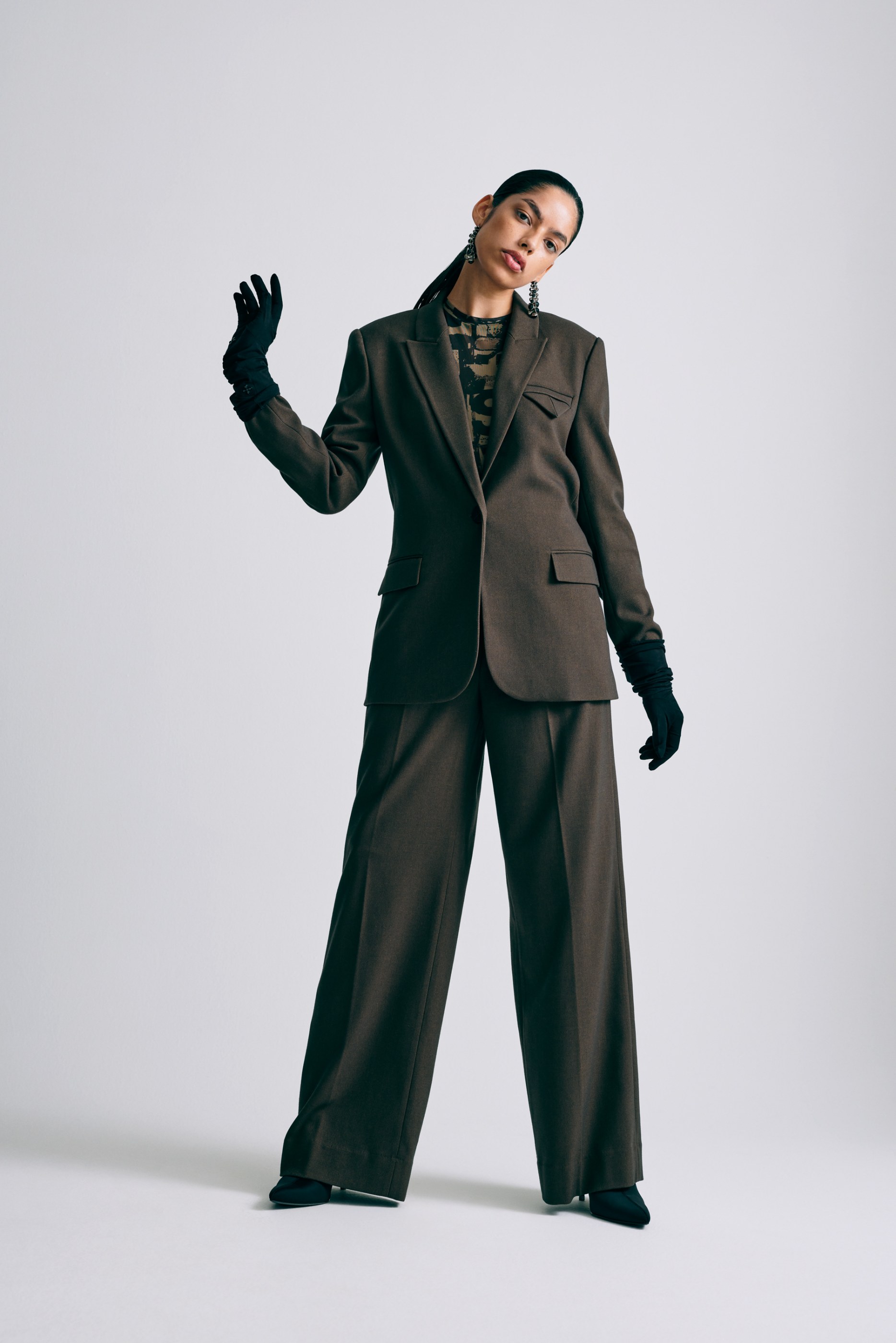 Woman in a dark brown suit, patterned top, and black gloves posing in studio.