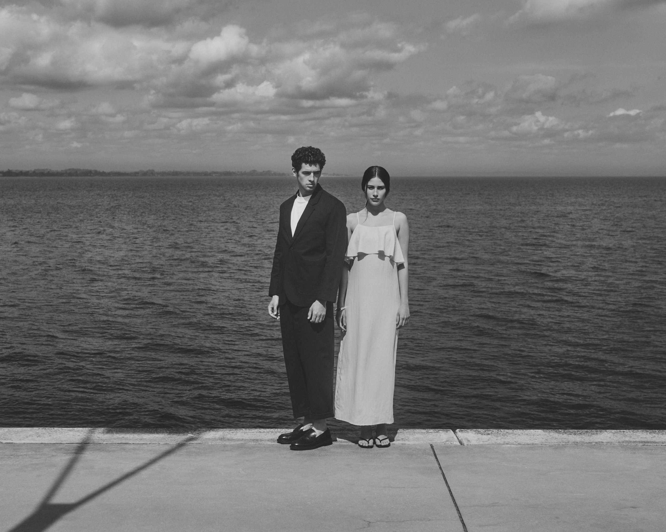 Black and white portrait of a man and woman standing on a pier by the ocean.
