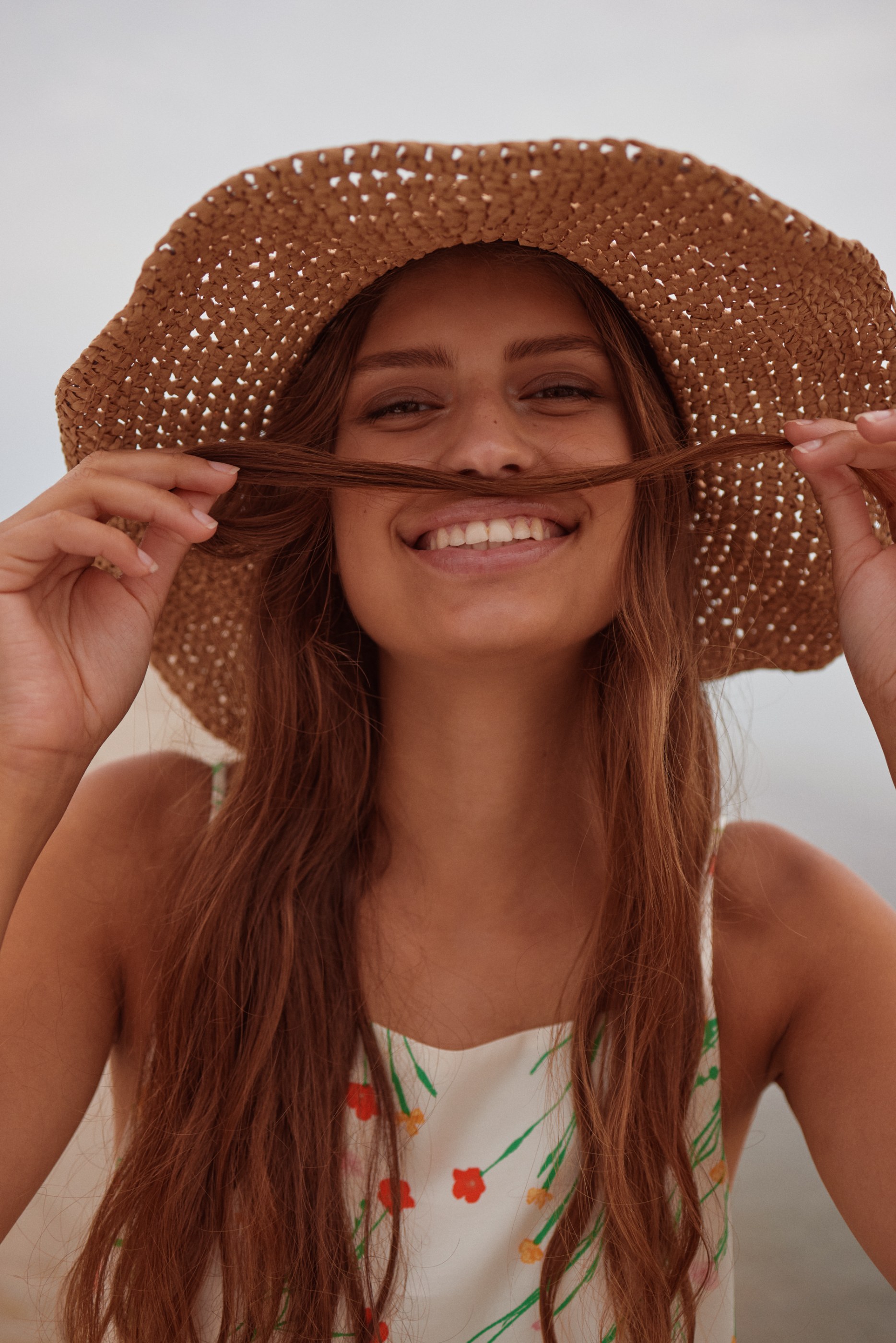 Close-up of a smiling woman in a straw hat holding her hair like a mustache.
