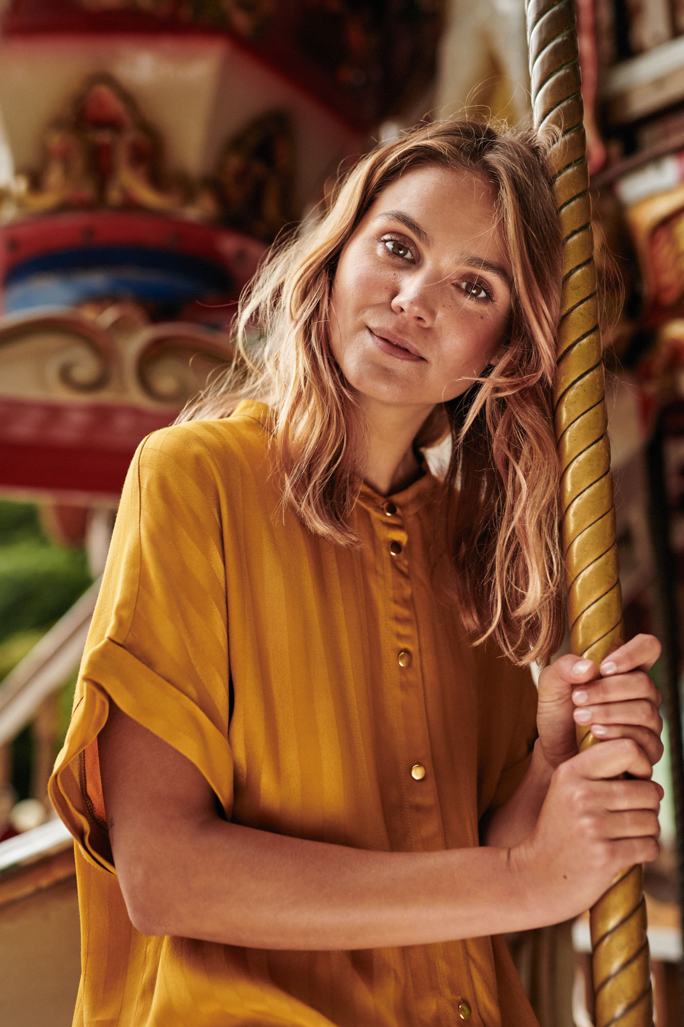 Smiling woman in a mustard yellow striped shirt holding a golden carousel pole.