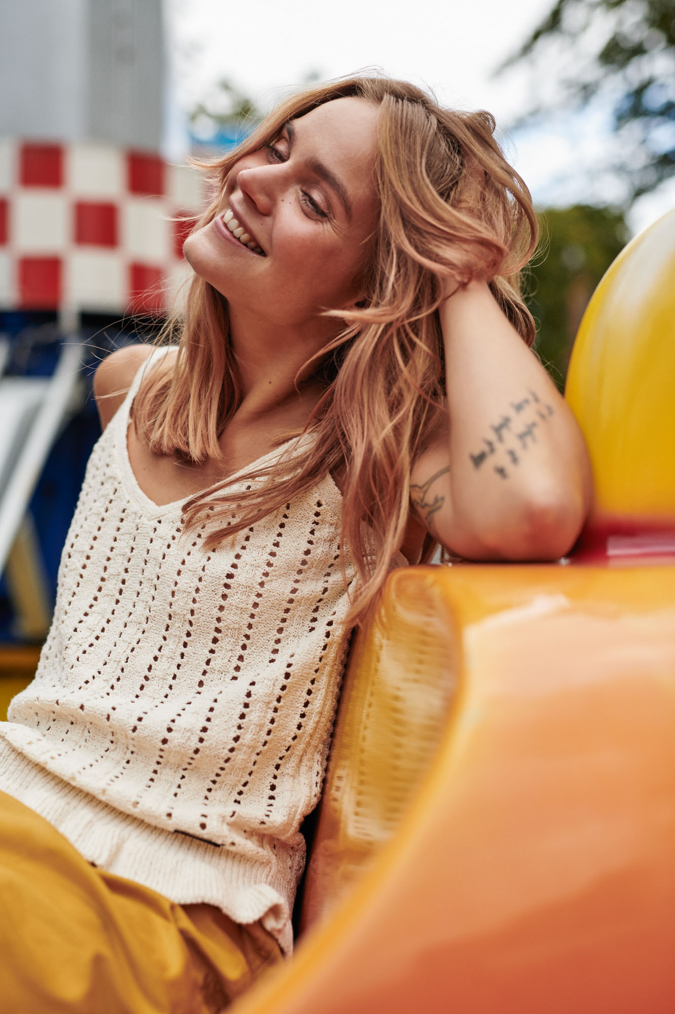 Smiling woman in white knit top and yellow pants, leaning on a yellow ride.