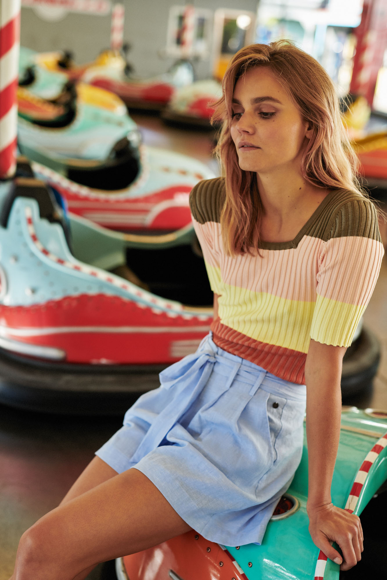 Thoughtful woman in a colorful striped top and blue shorts, sitting on a bumper car.