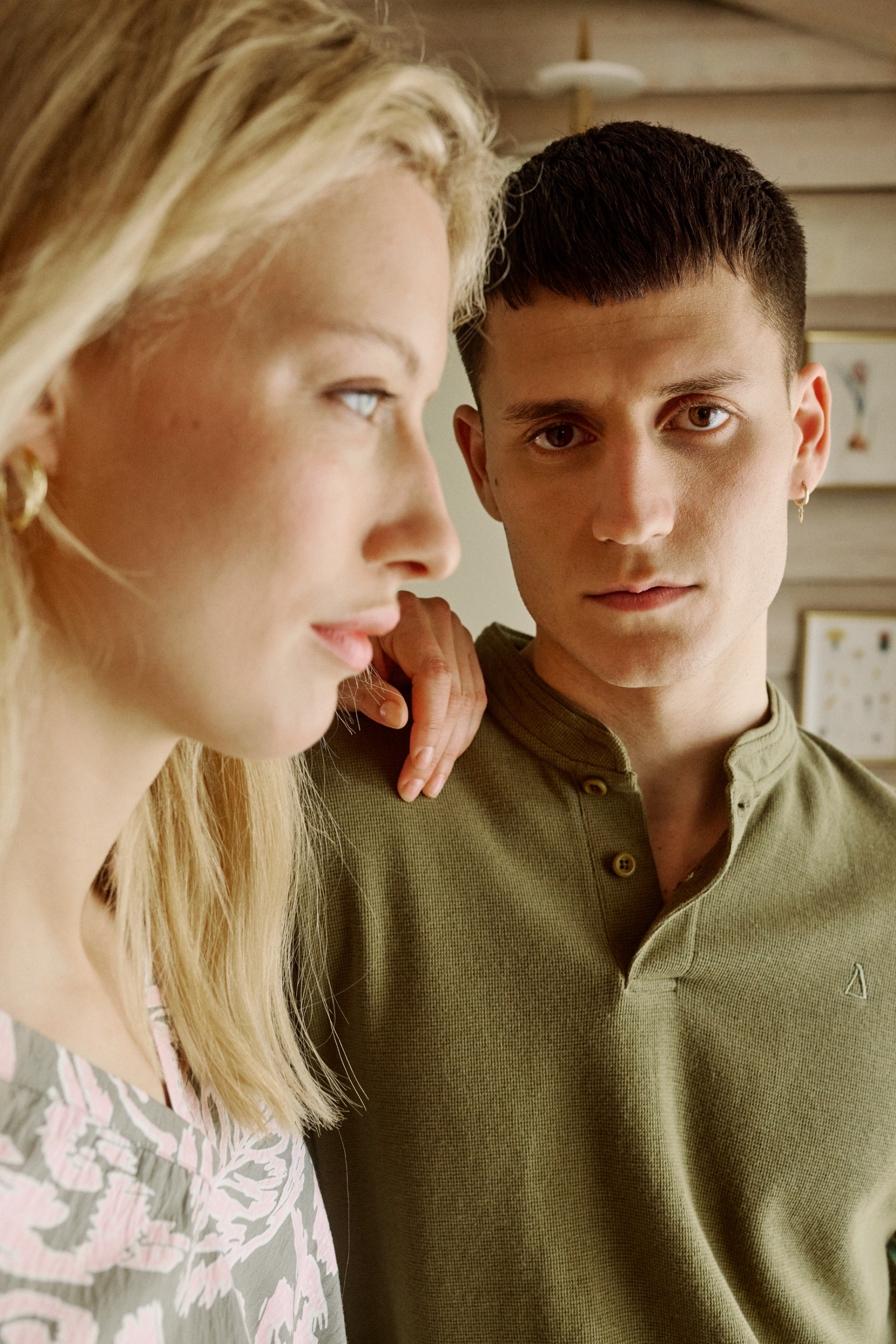 Intimate portrait of a blonde woman in profile, hand on a man's shoulder, he gazes forward.