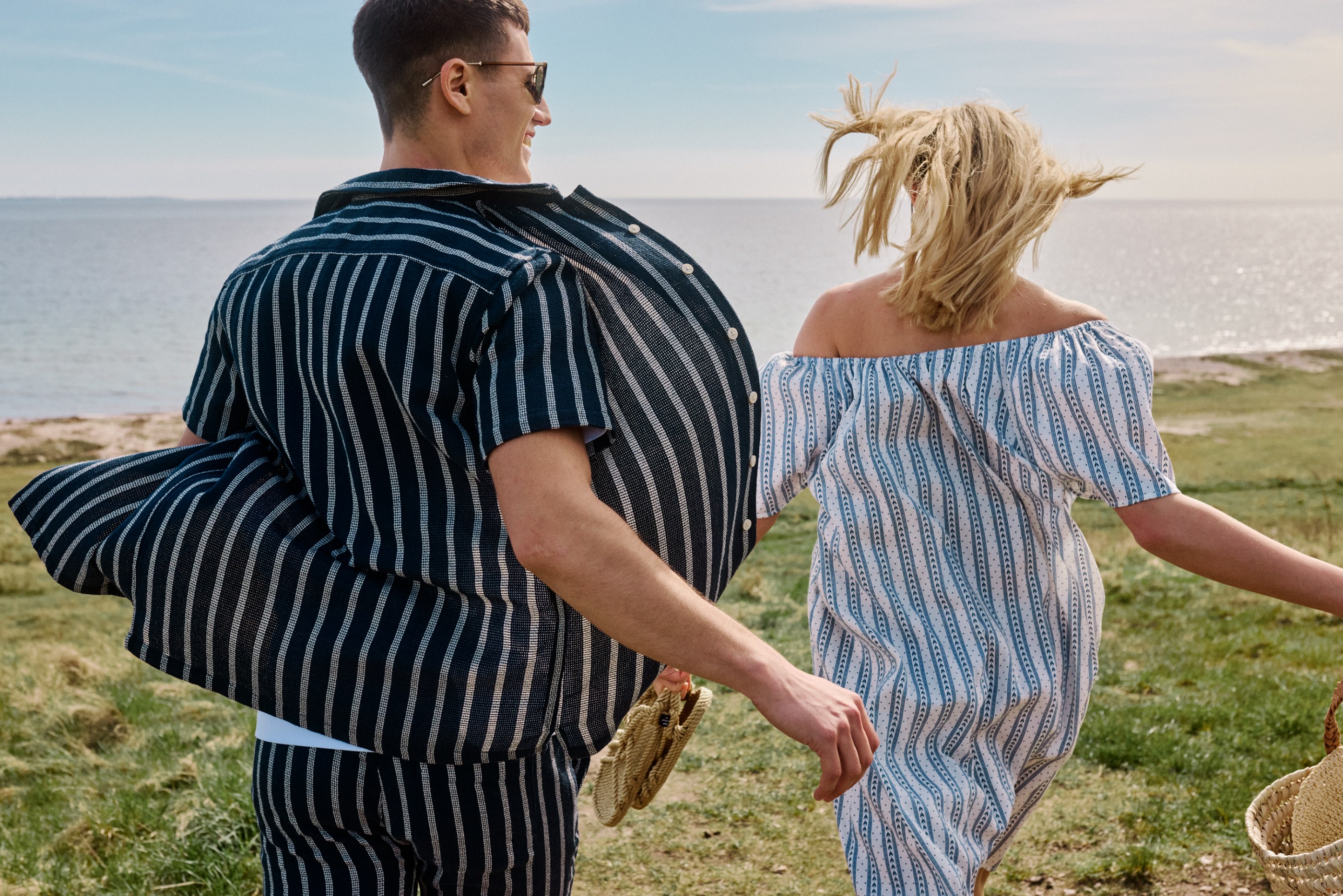 Joyful couple in striped outfits running towards a sparkling ocean.