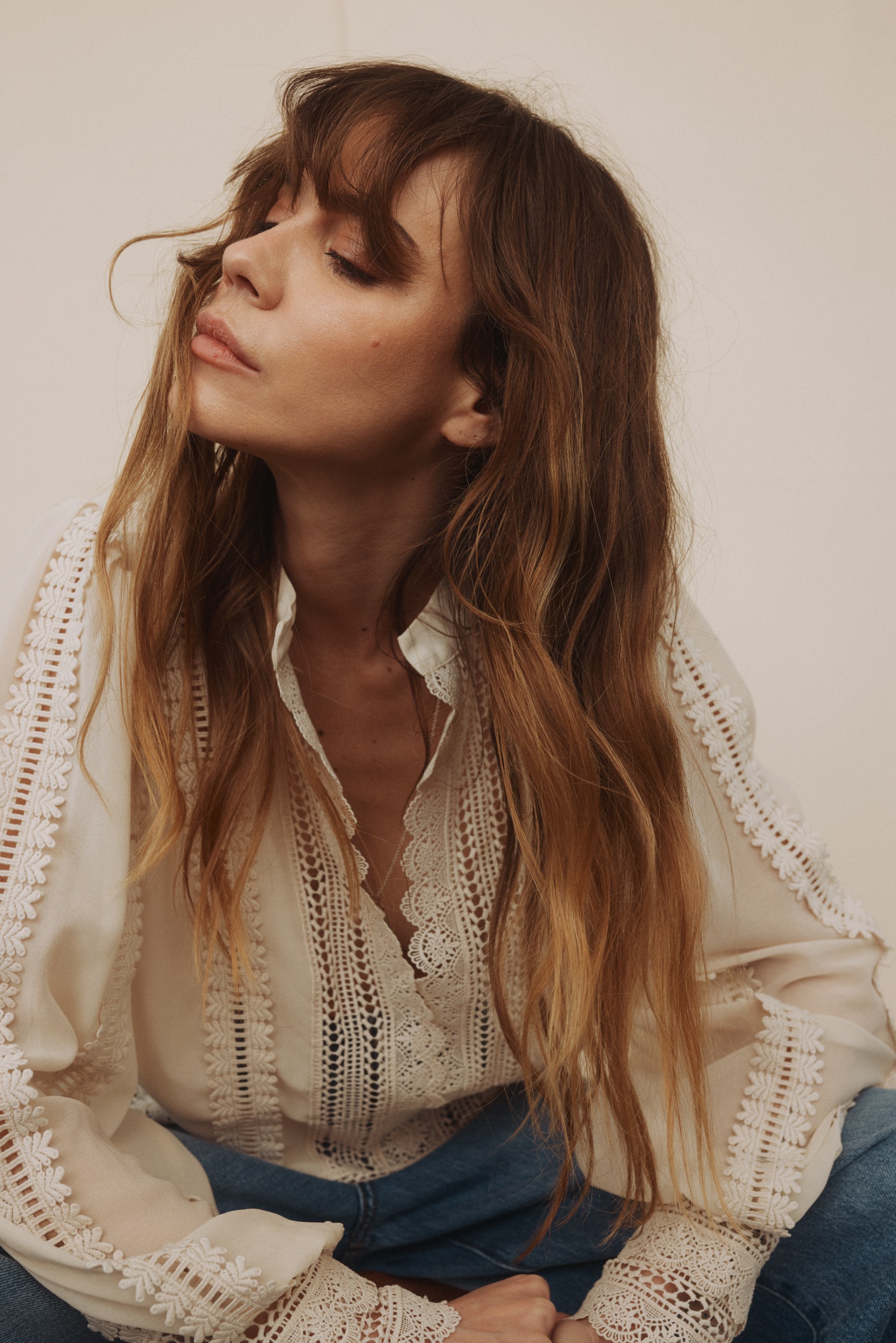 Woman with eyes closed, head tilted back, showing long brown hair and a white lace blouse.