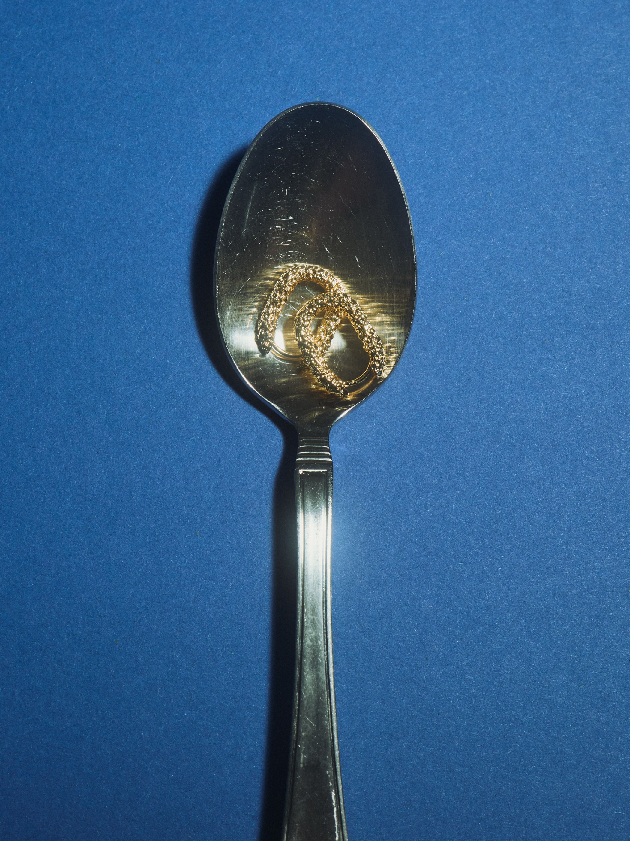 A silver spoon holding a textured gold, coiled object on a blue background.
