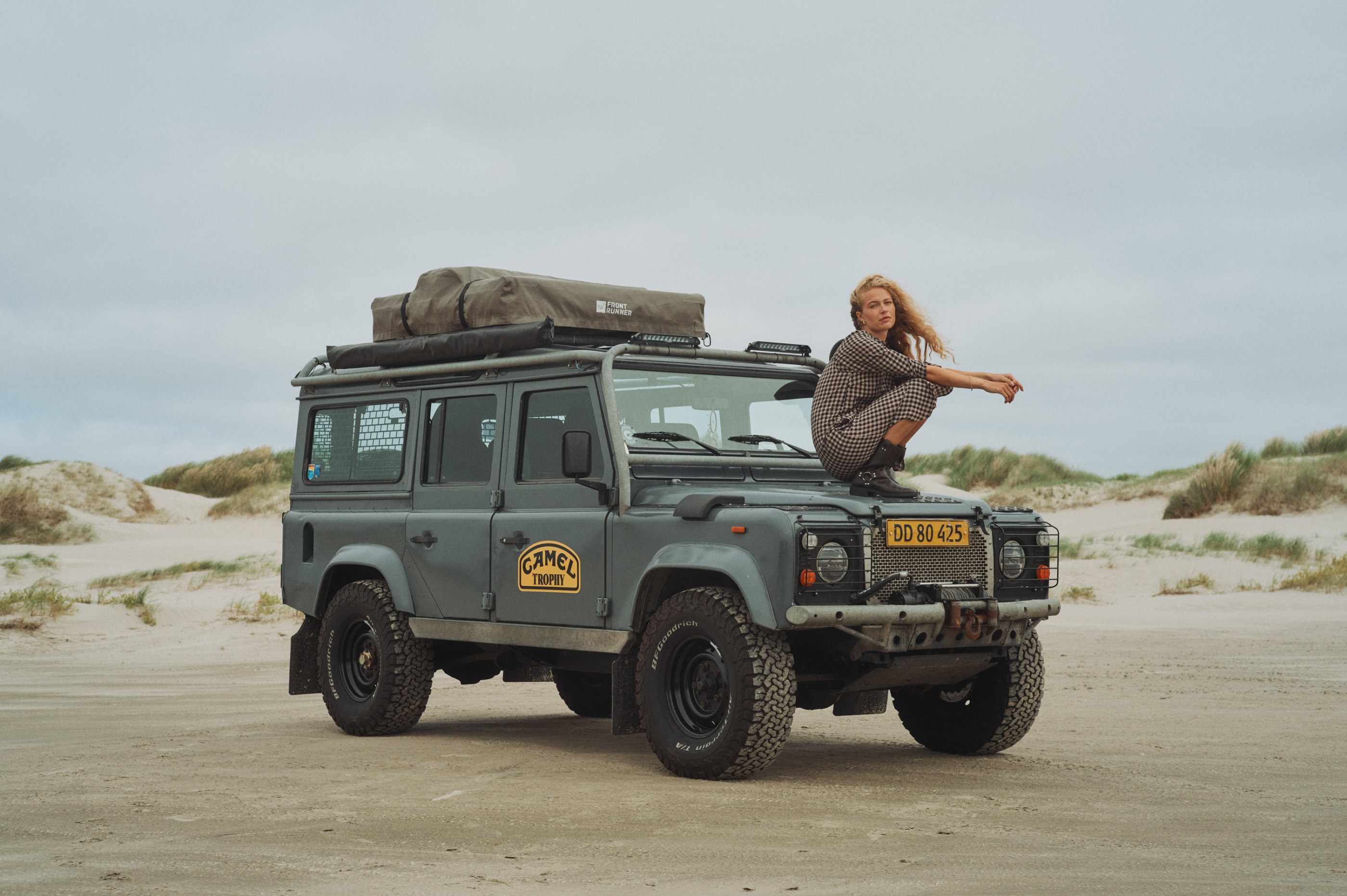 Woman in a plaid dress squatting on a grey off-road vehicle on a sandy beach.