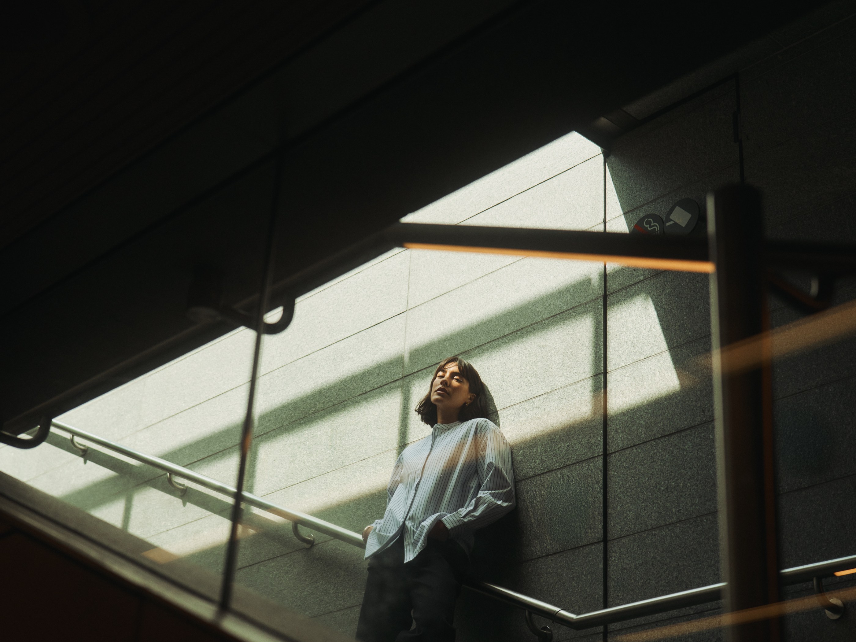 Woman in striped shirt leaning on a textured wall, illuminated by strong diagonal sunlight.