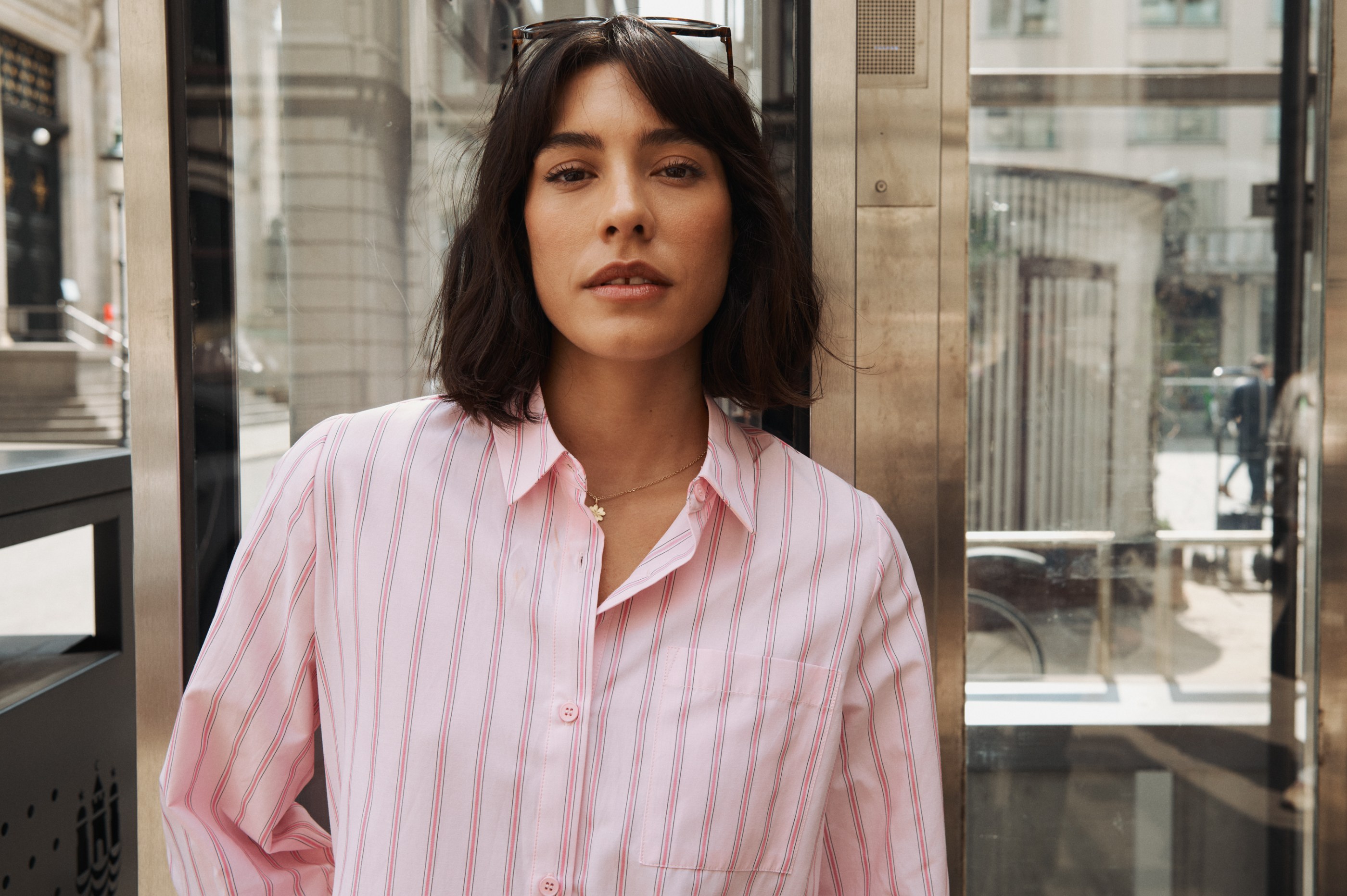Woman in a pink striped shirt and necklace, standing outdoors and looking at camera.
