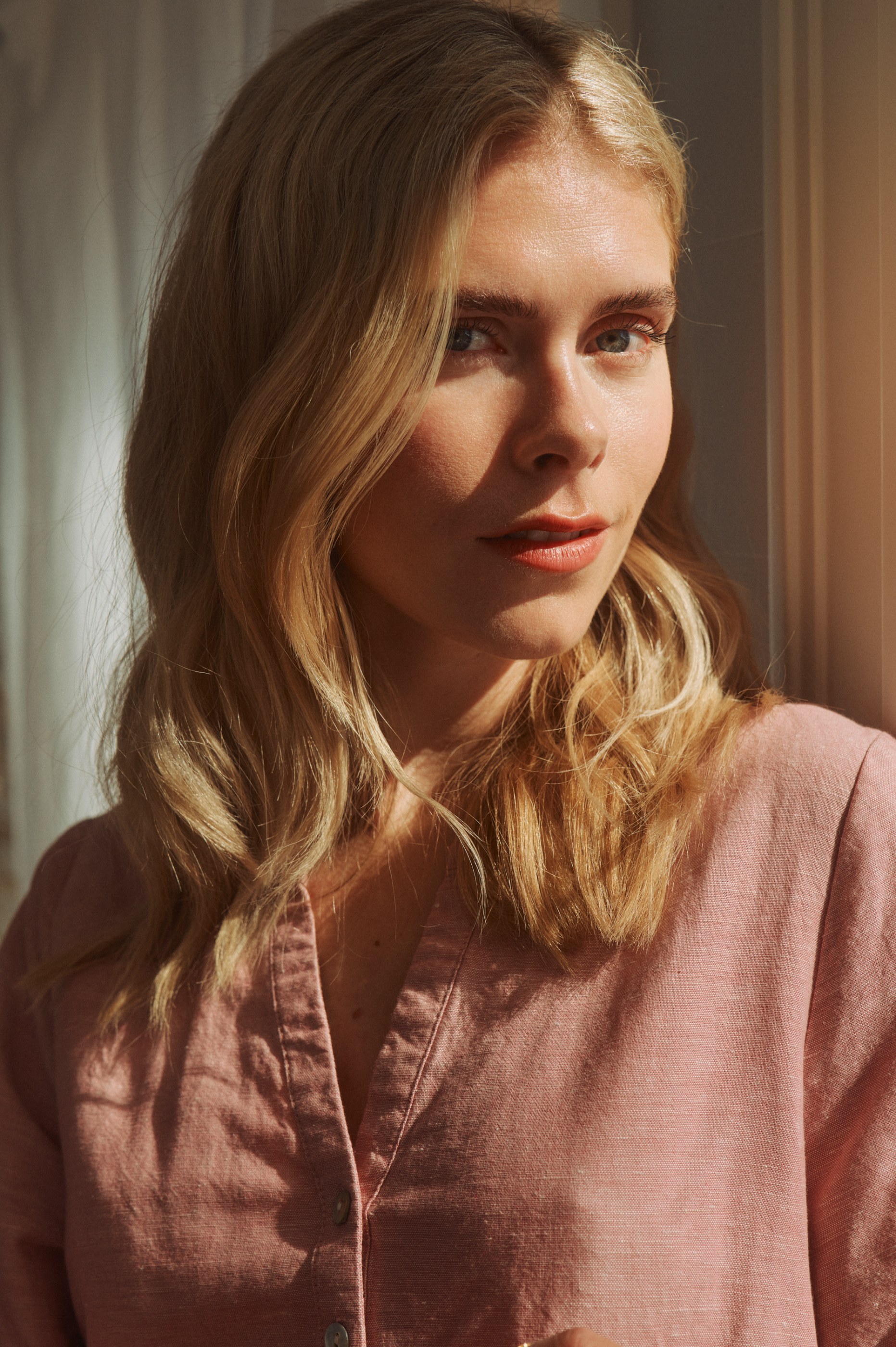 Portrait of a blonde woman in a pink shirt, bathed in warm side light.