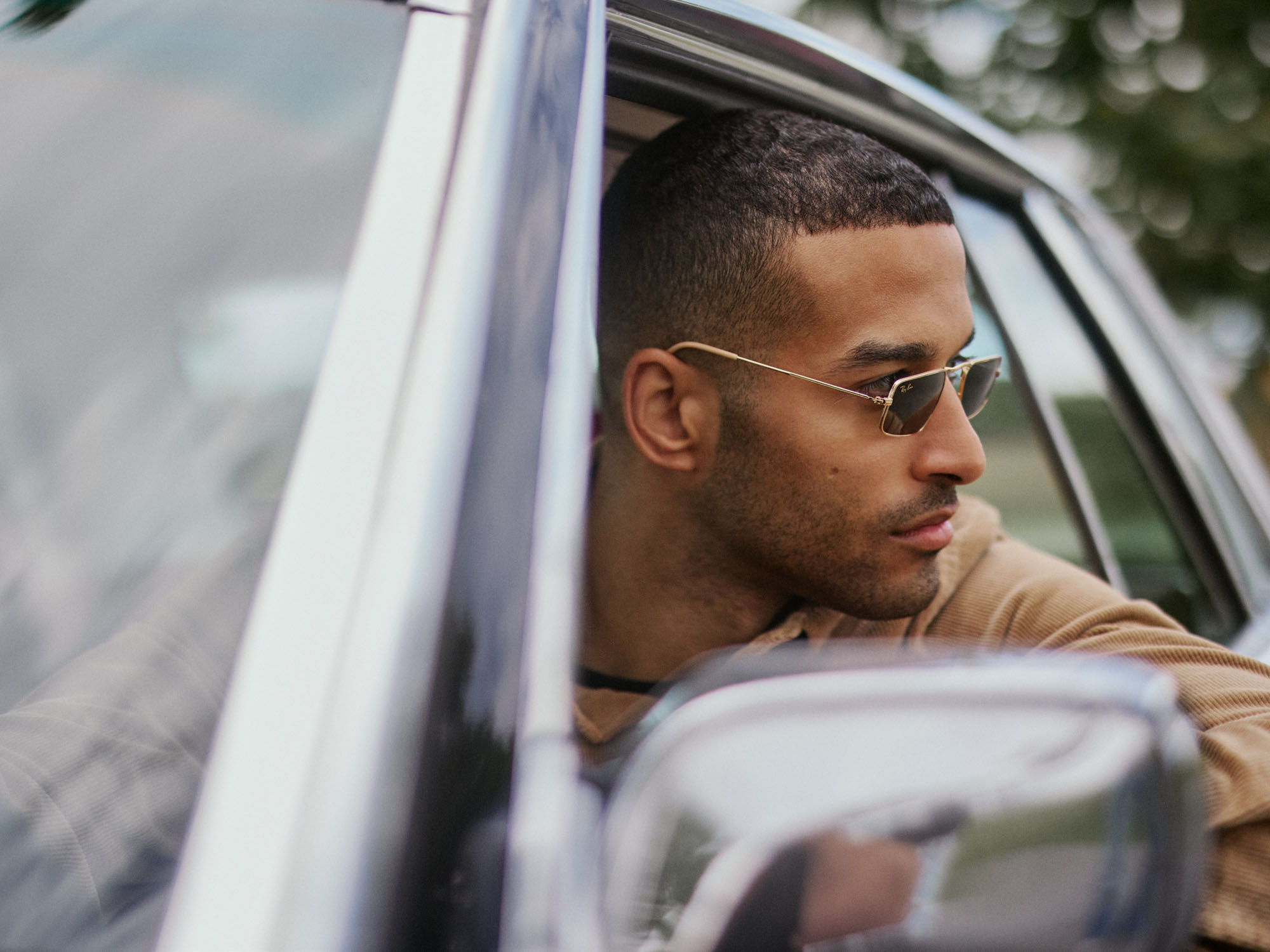 Man in Ray-Ban sunglasses and a tan corduroy shirt looking out a car window.