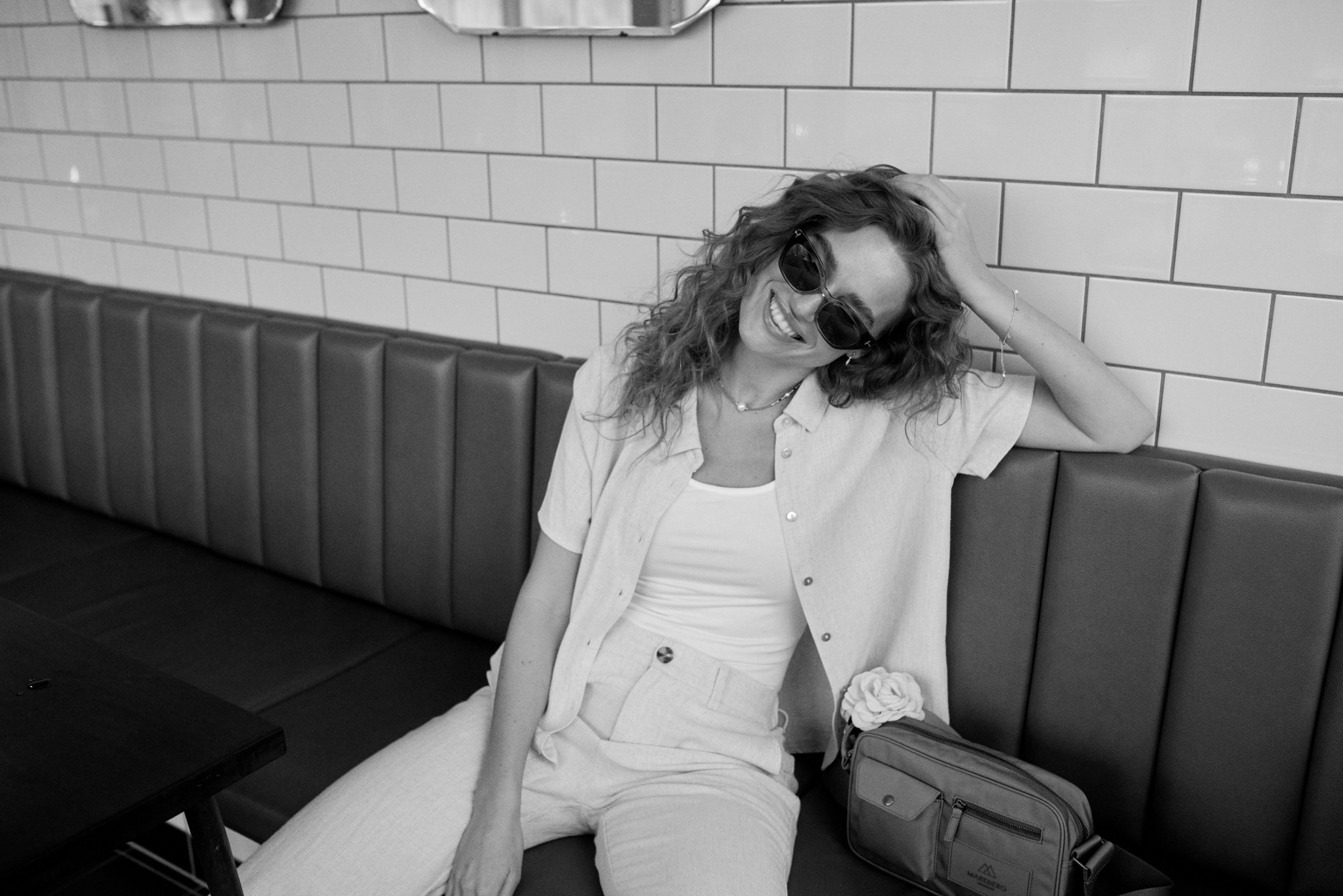 Smiling woman with curly hair and sunglasses relaxing in a restaurant booth.