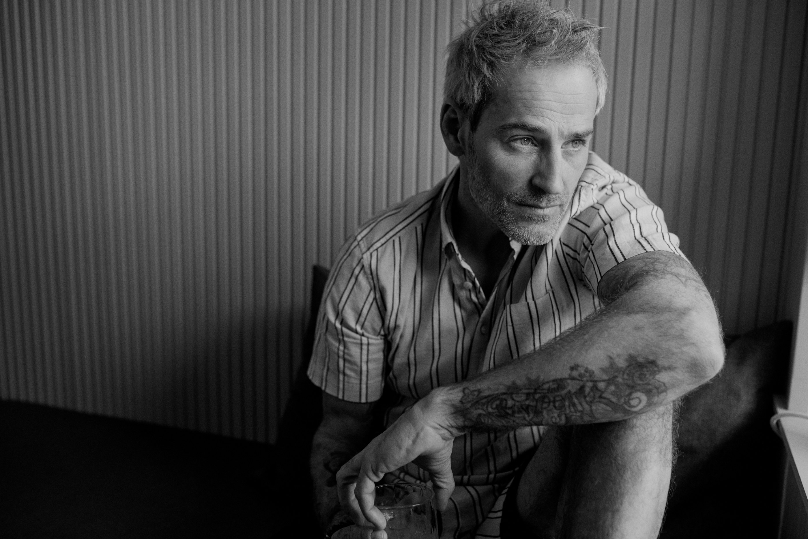 Black and white portrait of a thoughtful man with grey hair and a tattooed arm.